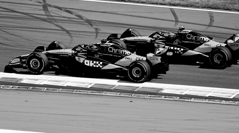 Two Formula 1 cars racing wheel to wheel, both covered in sponsor logos