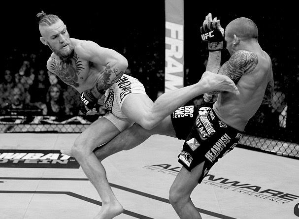 Two UFC fighters mid-exchange in the cage, sponsor branding on their shorts and the canvas